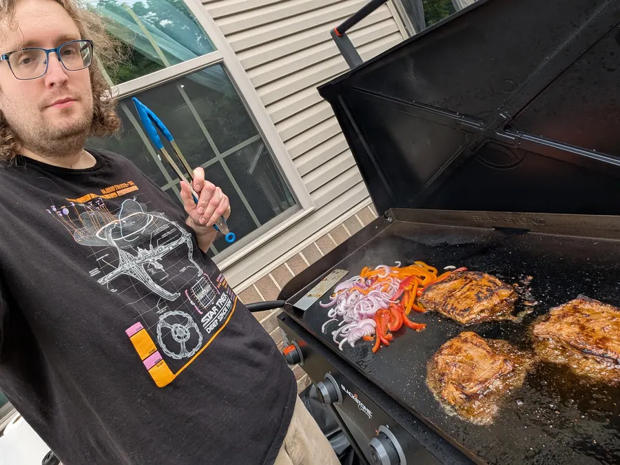 Food cooking on an outdoor griddle as Sean Talbot holds the tongs